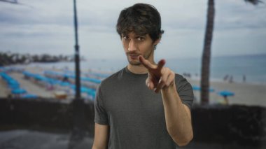 Adam deniz kenarındaki kumlu kıyılara ve okyanus manzaralı şemsiyelere el işareti yapıyor..