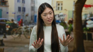 Bulanık arka planda sakin bir şekilde el kol hareketi yapan kadın, sakin ve barışçıl bir ifadeyi vurgulayan Asyalı bir şehir ortamına işaret ediyor..
