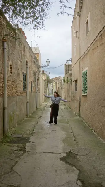 Mallorca 'da taştan binalarla kaplı, büyüleyici bir sokakta yürüyen bir kadın hafif bulutlu bir gökyüzünün altında huzurlu bir Akdeniz atmosferi yayıyor..
