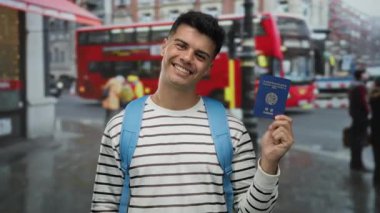 Elinde Kore pasaportu olan, arka planda kırmızı otobüsü olan, çizgili ve mavi sırt çantalı bir adam gülümsüyor..