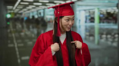 Kırmızı mezuniyet elbisesi giymiş, iç mekan ortamında gülümseyen, eğitim ve mezuniyetteki başarıyı sembolize eden, yoğun bir çevredeki insanlarla çevrili bir kadın..