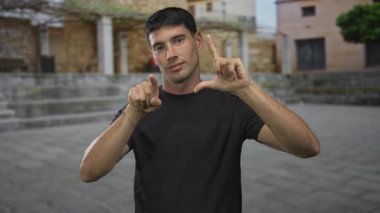 Latin kökenli genç adam, tarihi taş binaların arasında eski şehir sokağında eli boş bir hareket sergiliyor..