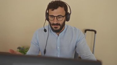 Ofiste kulaklıklı bir adam bilgisayara bakarken stresli bir şekilde başını tutarak iş sorunlarını ve ofis baskısına yoğunlaşmayı öneriyor..