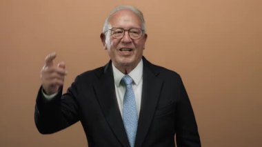 Takım elbiseli kıdemli bir adam kahverengi izole edilmiş bir arka plana karşı enerjik bir şekilde konuşuyor ve işaret ediyor..