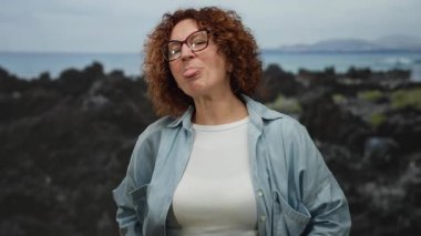 Açık havada bulutlu bir günde deniz kenarında esmer bir kadın neşeli bir şekilde gülümsüyor..