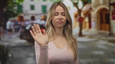 Sarışın beyaz kadın, alışveriş merkezleri ve ağaçlarla dolu kalabalık bir Avrupa caddesinde sağ işaret parmağını kameraya doğrultarak uyarı uyarısı yaptı.