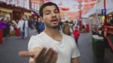 Ciddi ifadeye sahip bir adam uzanmış elleriyle ve renkli caddede işaret ederek işaret ediyor; davet bağlantısı.