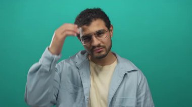 Gündelik gömlekli İspanyol genç adam yeşil arka planda el ele stüdyoya dokunuyor; kafa karışıklığı benlik yansıması.