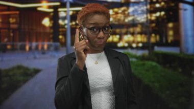 Kadın, gece işlek şehir caddesinde parmağı şakağına gösteren dürbünlü el hareketi yapıyor..