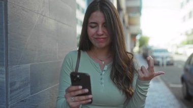 İspanyol kadın akıllı telefonu açık havada mutlu bir şekilde kullanıyor, neşe ve memnuniyeti ifade ediyor, teknolojiyle ilgileniyor..