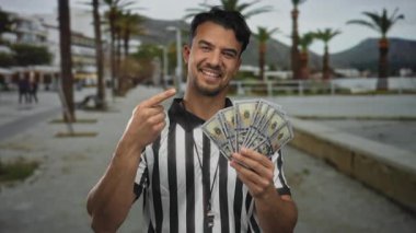 Genç İspanyol hakem, arka planda zenginliği ve başarıyı sembolize eden insanlar ve palmiye ağaçları olan bir şehir caddesinde bize dolar yağdırıyor..