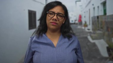 Kadın, güneşli beyaz bir şehir caddesinde siyah gözlüklü şaşılarla, kepenkleri kapalı ve taş saksılarıyla karşılaşıyor..