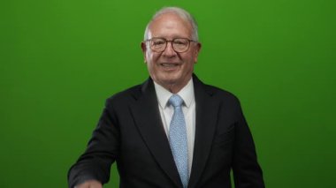 Takım elbiseli kıdemli adam patronun suratını tutuyor ve yeşil arka plana kaya hareketi yapıyor. Güvenini ve otoritesini gösteriyor..