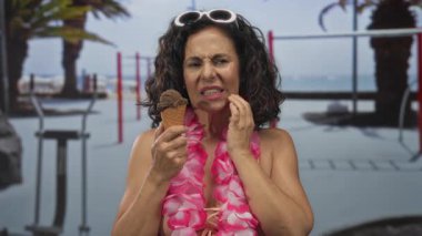 Orta yaşlı İspanyol kadın spor merkezinde yanaklarına dokunurken çikolatalı dondurma külahını tutuyor; diş ağrısı hayal kırıklığı acısı.