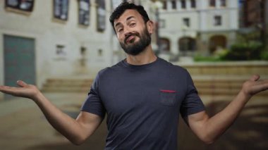 Sokakta sakallı İspanyol bir adam sorgulama jestinde elleri açık duruyor, bulanık şehir geçmişiyle kameraya güvenle gülümsüyor..