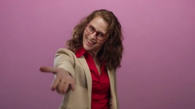 İş kıyafetleri içinde gülümseyen bir kadın canlı pembe bir arka plana uzanır. Güven ve dostluk yayar.