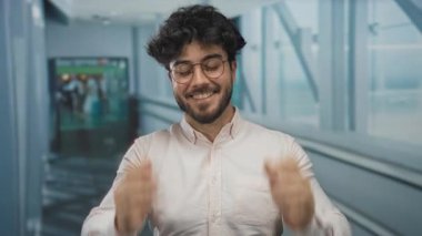 Young man with beard and glasses smiling indoors at an airport, illustrating travel ambiance and excitement in a contemporary setting.