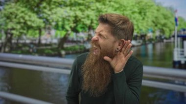 Kızıl sakallı bir adam kıs kıs bakıyor ve kanalın korkuluklarında el ele tutuşuyor..