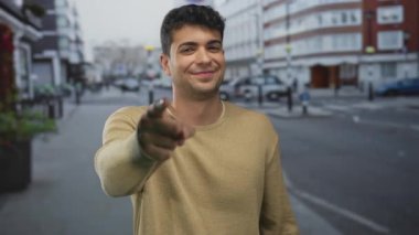 Adam parmaklarını yukarı doğru renkli arka planda tutarak dokunuyor, genç erkek İspanyol gülümsemeli süveter pozu veriyor.