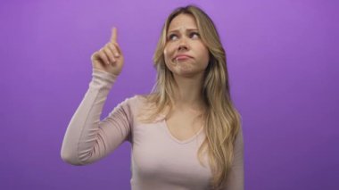 Sarışın beyaz kadın stüdyo ortamında işaret parmağını yukarı kaldırıyor; şüphecilik onaylanmayan çelişki tereddüdü.
