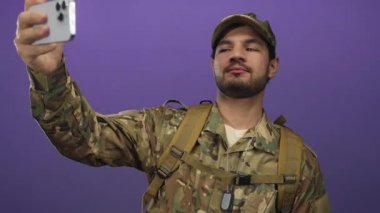 Kamuflaj üniforması giyen İspanyol asker mor stüdyoda akıllı telefonu kolunda tutuyor..