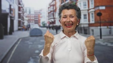 Gri saçlı, gülümseyen ve kameraya öpücük yollayan yaşlı bir kadın. Kırmızı tuğlalı binalar gün içinde dışarıda neşe ve şefkat gösteriyor..