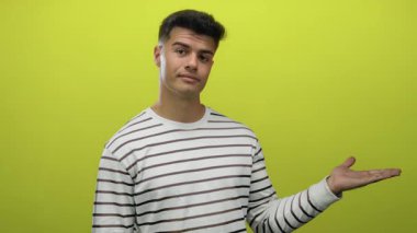 İzole edilmiş sarı arkaplan karşısında avucunun içi açık gülümseyen İspanyol genç adam sunum kavramını ima ediyor