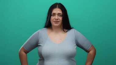 Uzun saçlı, yeşil arka plan duvarına karşı duran, rahat giyinen, kıvrımlı, genç bir kadın..