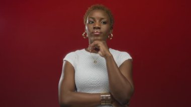 Eli çenesinde ve önkolunda altın halka küpeler ve kırmızı stüdyo ortamında beyaz bluz giyen bir kadın..