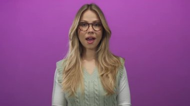 Sarı saçlı ve yuvarlak gözlüklü kadın, stüdyoda çene yakınında ellerini çırpıyor; umarım şefkat sıcaklığı dinginliği.