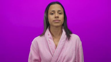 Bornoz giymiş bir kadın pembe bir arkaplana karşı kafasına jest yapar, neşeli, tuhaf bir ifadeyle canlı ve izole bir şekilde düşüncelerini ya da farkındalığını aktarır..