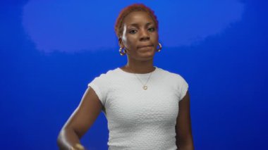 Kırmızı manikürlü ve altın küpeli bir kadın stüdyoda işaret ve orta parmaklı barış işareti taşıyor..