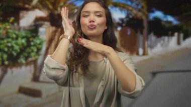 İspanyol genç kadın, güneşli bir sokak köşesinde iki eliyle yüzünü çerçeveler; yaratıcı vizyon.