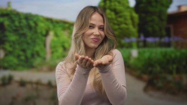 Kadın gülümser ve avuçlarını açık tutarak güneşli yeşil parkta öne bakar; samimiyet davetkarlık bağlantısı.