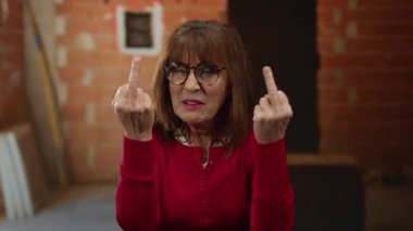 Üst düzey İspanyol kadın inşaat alanında orta parmaklarını gösteriyor. Duvarın arkasında haylaz bir ifade var..