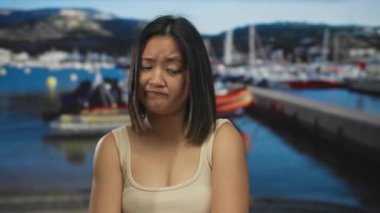 Deniz kıyısındaki bir limanda genç bir kadın, tekne ve denizle ilgili dalgın bir görünüm sergiliyor, denizcilik ortamında duygusal bir anı yansıtıyor..