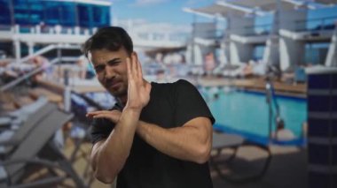 Bir yolcu gemisindeki genç İspanyol adam arka planda bir yüzme havuzu ve güneşlenme yerleriyle korku gösteriyor. Tatil endişesi ve açık hava seyahati duygularını tasvir ediyor..