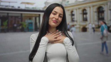 Açık havada gülümseyen, uzun siyah saçlı, şehir ortamında beyaz gömlek giyen, tarihi mimarinin bulanık arka planına sahip ve yürüyen insanlar..