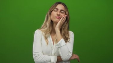 Sarışın genç bir kadın, bir fotoğraf stüdyosunda başını dinlendirirken elini yanağına uzatıp kolunu çapraz yapar..