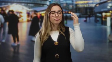 Gözlüklü bir kadın şehir manzarası arka planı bulanık ve akşamları renkli ışıkları olan hareketli bir caddede dolanıp duruyor..