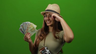 Kamera ve Peru tabanlı bir kadın canlı yeşil bir arka plana karşı neşeli bir şekilde poz veriyor. Hasır şapka takıyor ve neşeli hareketler yapıyor. Neşeli bir seyahat havası yakalıyor..