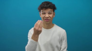 Gözlüklü genç adam stüdyo ortamında beyaz gömlek giyerek parmak hareketi yapıyor..