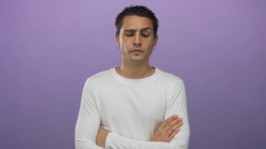 Kollarını kavuşturmuş İspanyol bir adam ve izole edilmiş mor bir stüdyoda beyaz gömlek giyen tarafsız bir yüz ifadesi..