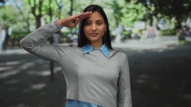 Açık hava parkında selam veren bir kadın güneşli bir günde bulanık bir arka plana karşı güven ve saygı taşıyor..