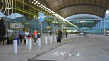 Havaalanı 1 taksi terminalinde bavulları olan erkekler ve kadınlar da dahil olmak üzere yolcuların bulanık görüntüsü, hareketi ve modern dış çevreyi vurguluyor..