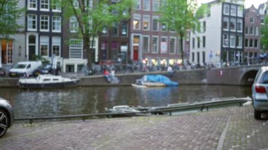 Amsterdam Kanalı 'nın teknelerle ve geleneksel Hollanda evleriyle bulanık görüntüsü sakin bir şehir arkaplanı yaratıyor ve yumuşak gün ışığında bokeh etkisini dağıtıyor..