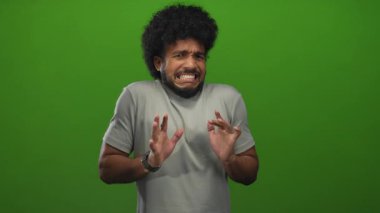 Yeşil arka plan önünde tiksindiğini ifade eden bir adam, kapalı alanda izole edilmiş, günlük gri bir gömlek giyen, duygusal, anlamlı, esprili ve komik bir tepki gösteren bir adam..