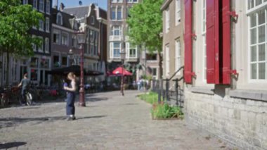 Tarihî binalar, yemyeşil alanlar ve Amsterdam, Hollanda 'da bisikletlerle büyüleyici bir kaldırım taşı caddesinde duran bir kadının odaksız manzarası..