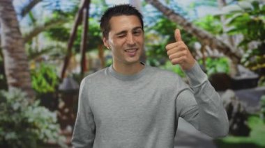 Genç ispanyol adam ağaçların arasında duruyor ve ormanda baş parmak işareti yapıyor..