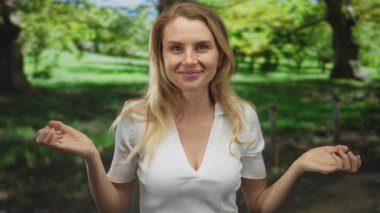 Açık yeşil bir parkta gülümseyen bir kadın, neşe ve rahatlığı açık kollarıyla ifade ediyor, aydınlık doğa ve güneşli bir gökyüzünün altında canlı ağaçlarla çevrili..